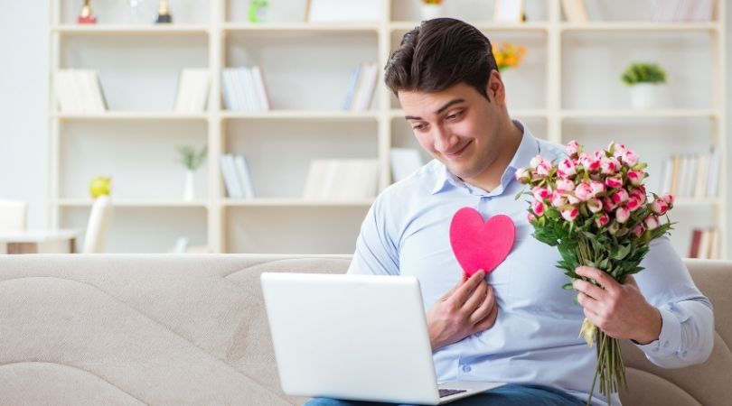 man holding flowers and heart talking through a computer